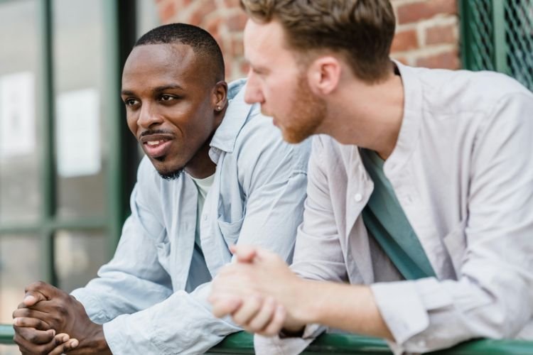 Two men are talking and offering emotional support to each other. Leaning into emotions is a part of wedding wellness for grooms.