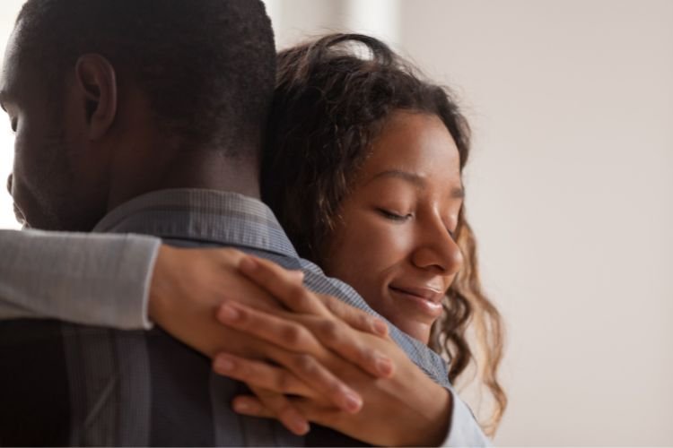 A woman hugs a man. Talking about mental health with your partner is an important part of a groom’s wedding wellness.