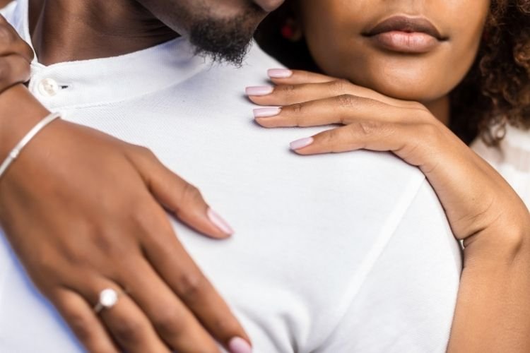 A woman wearing an engagement ring wraps her arms around her fiancé.